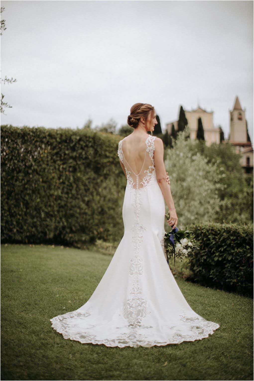 Bride in her lace gown overlooks a castle while holding her bouquet.
