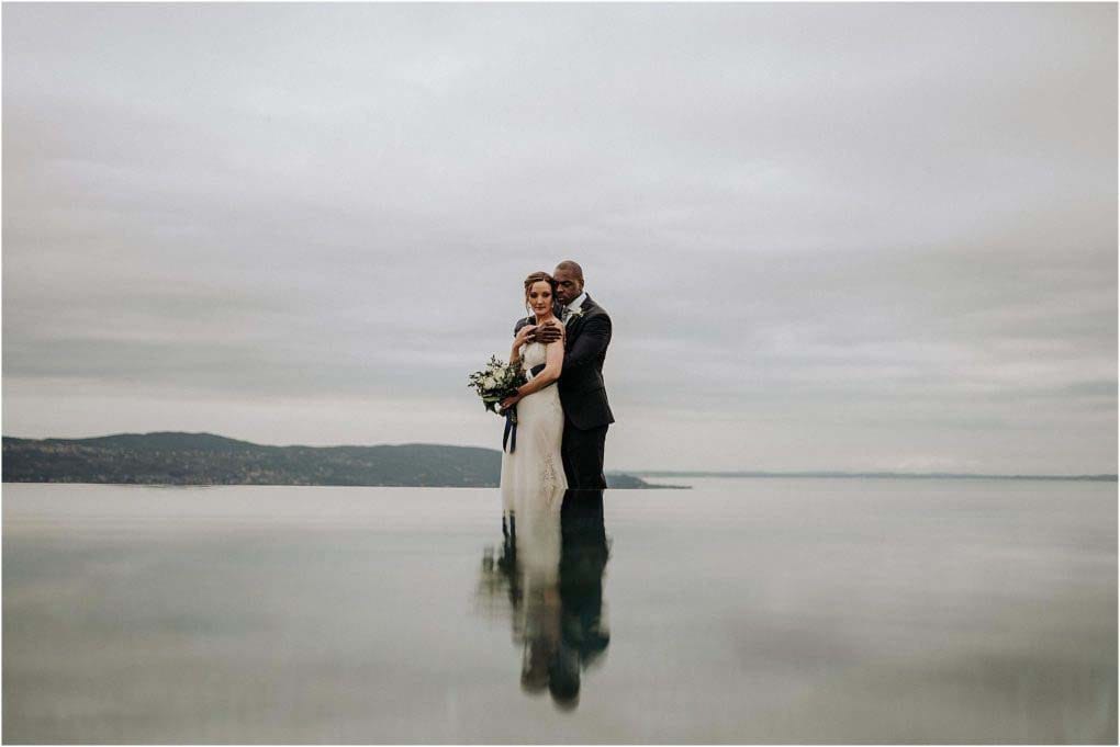 Bride and groom pose with their reflection in the lake.