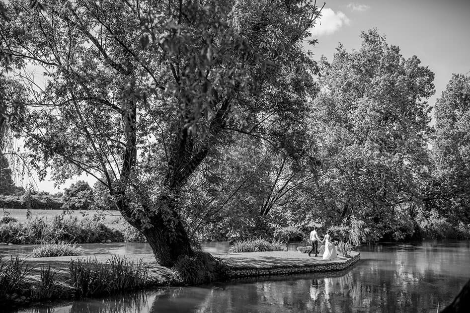 Black and white photo of bride and groom walking together by the lake.