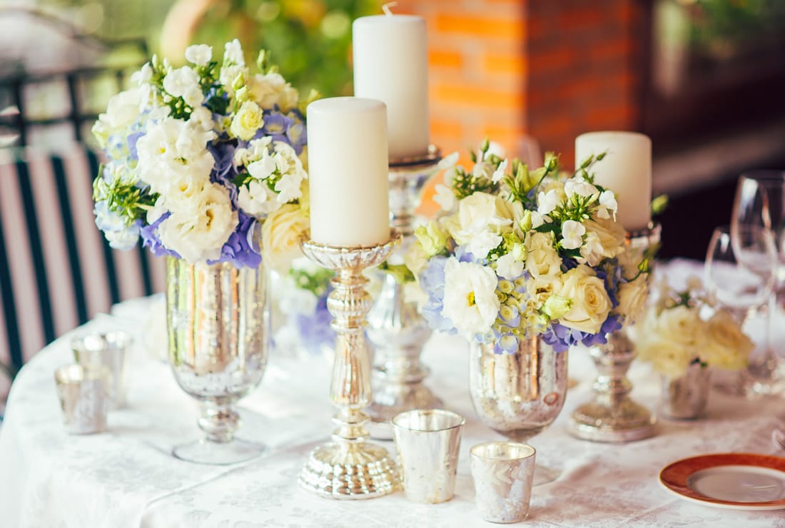 A wedding reception table design. With silver vases, candles and white and purple flowers.