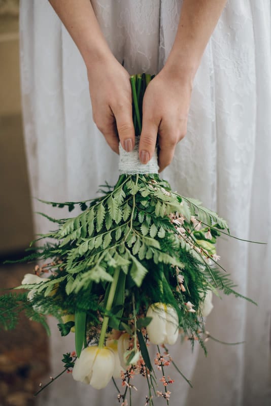 Bride holding her bouquet downward. It is full of greenery and white flowers.